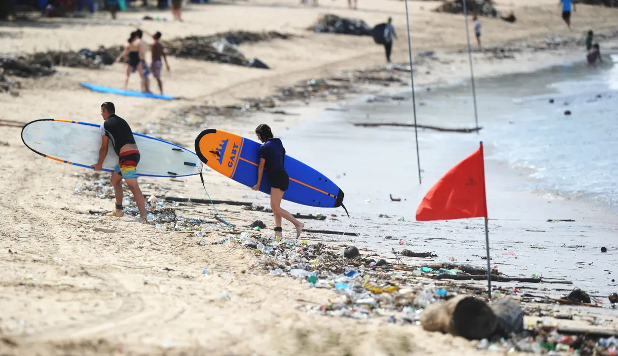 Turis berjalan dengan papan selancar melintasi puing-puing dan sampah di pesisir Pantai Kuta, Bali, Minggu (9/12). Kawasan pantai Kuta kembali dipenuhi oleh sampah hanyut terbawa oleh gelombang. (SONNY TUMBELAKA / AFP)