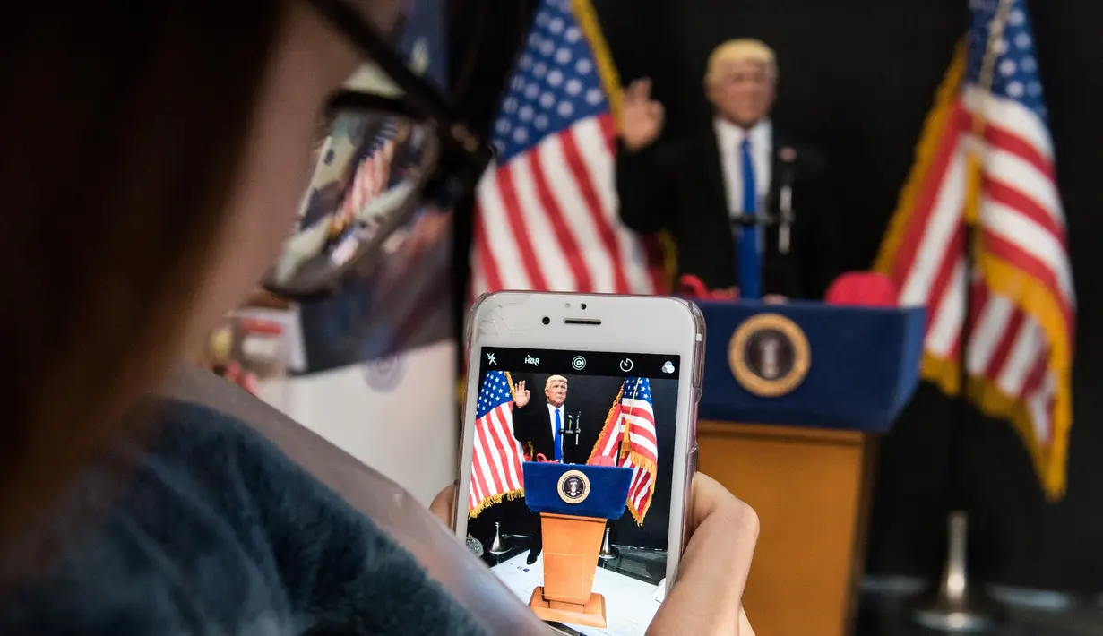 Pelanggan mengabadikan boneka Donald Trump saat berpidato di toko mainan, Hong Kong (3/2). Pembuat boneka di Hong Kong yang sering menciptakan boneka pemimpin dunia yang kontroversial telah membuat patung Donald Trump. (AFP Photo/Anthony Wallace)