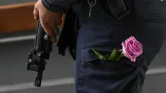 Seorang petugas polisi berjaga dengan bunga di sakunya saat orang-orang berkumpul untuk mengenang para korban di pintu masuk pusat perbelanjaan Field di Kopenhagen, Denmark, 5 Juli 2022. Polisi mengatakan seorang pria bersenjata yang membunuh tiga orang ketika dia melepaskan tembakan di pusat perbelanjaan yang ramai bertindak sendiri dan tampaknya memilih korbannya secara acak. (AP Photo/Sergei Grits)