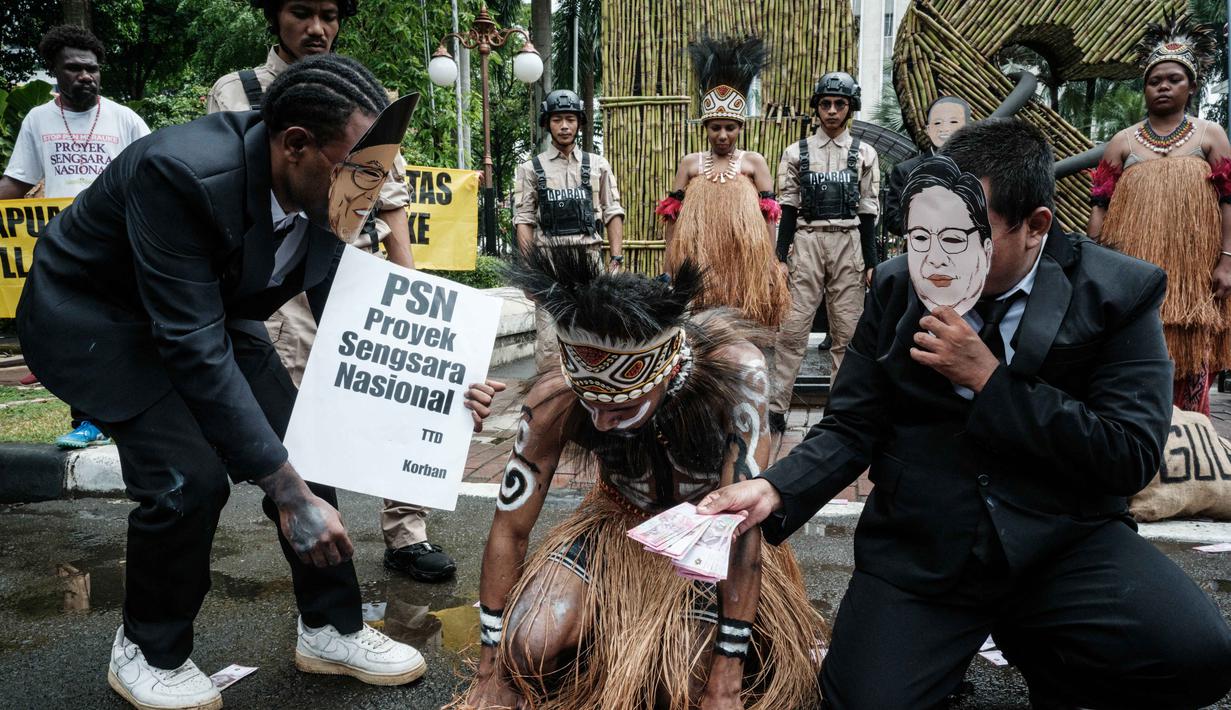 Mereka menyuarakan kritik terhadap ancaman deforestasi besar-besaran untuk Proyek Strategis Nasional (PSN) tebu di Merauke. Tampak dalam foto, aktivis Greenpeace Indonesia bersama beberapa pemuda Papua menggelar aksi teatrikal saat berunjuk rasa di depan Kantor Kementerian Koordinator bidang Perekonomian, Jakarta, Kamis (18/12/2025). (Yasuyoshi Chiba/AFP)