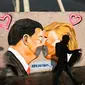 Seorang pria berjalan di depan Graffiti yang menggambarkan Presiden AS Trump (kanan) dan Presiden Tiongkok Xi Jinping saling berciuman dengan mengenakan masker di tembok taman umum Mauerpark di Berlin, Jerman, Rabu, (29/4/2020). (AP/Markus Schreiber)