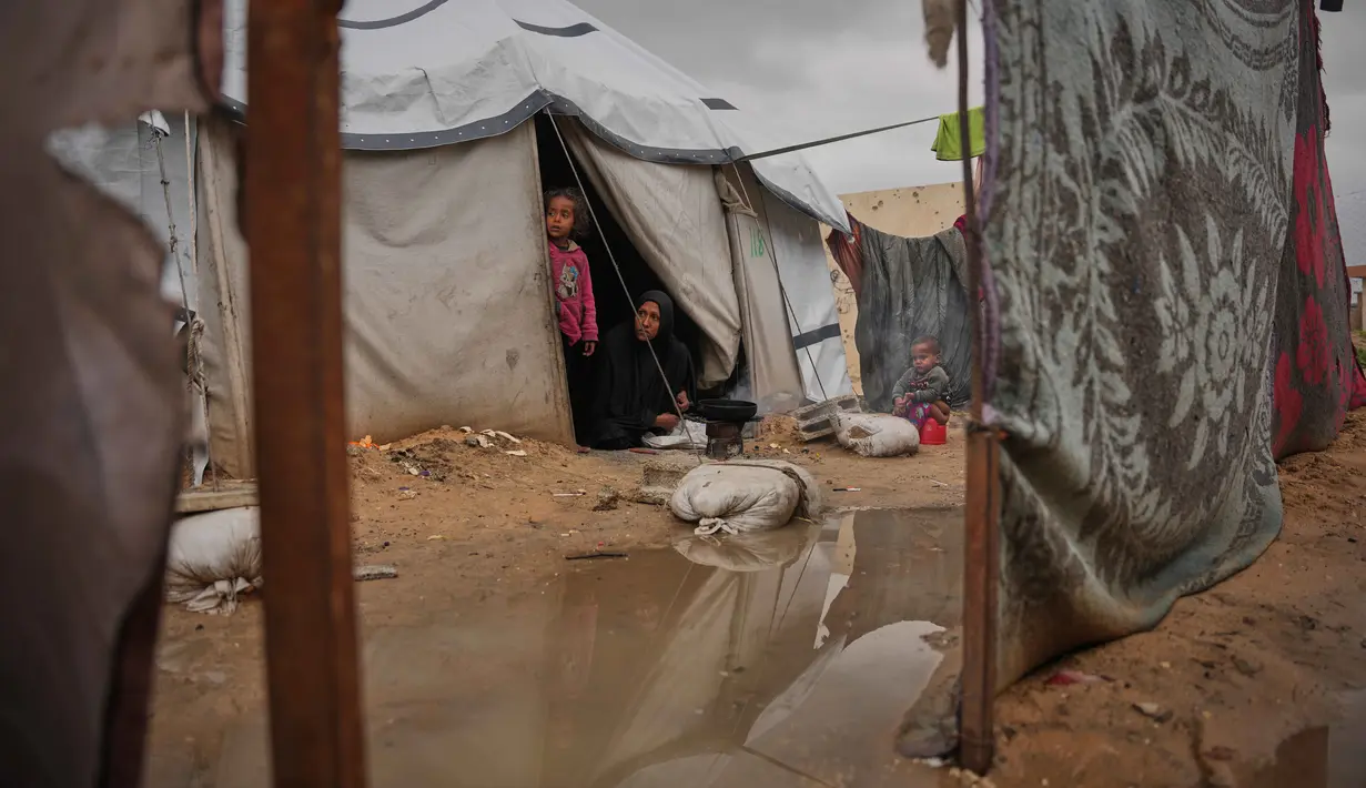 Nanaa Abu Jari memasak di luar tendanya setelah tenda tersebut terendam air hujan di Nuseirat, Jalur Gaza tengah, Jumat, 2 Januari 2026. Hingga awal Januari 2026, wilayah Gaza masih dihantam cuaca ekstrem yang memperparah krisis kemanusiaan di sana. (AP Photo/Abdel Kareem Hana)