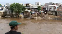 Warga berada di seberang pemukiman padat di bantaran kali Ciliwung, Jakarta, Kamis (16/4/2020).  Menko Bidang Perekonomian Airlangga Hartarto mengungkap proyeksi pemerintah terhadap angka kemiskinan naik dari 9,15 persen menjadi 9,59 persen akibat pandemi COVID-19. (Liputan6.com/Helmi Fithriansyah)