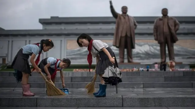 Para siswa membersihkan jalanan di depan patung pemimpin Korea Utara Kim Il Sung dan Kim Jong-Il di bukit Mansu saat negara tersebut menandai 'Victory Day' di Pyongyang (AFP/Ed JONES)