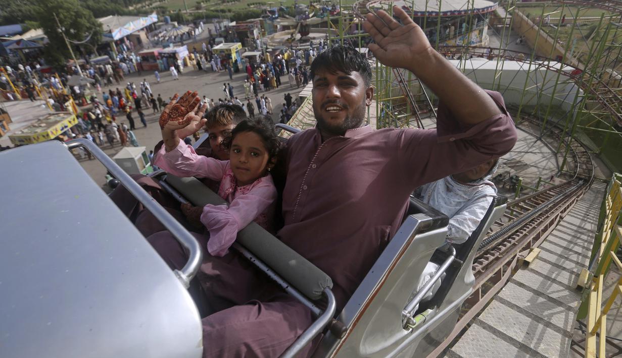 <p>Sebuah keluarga melambai sambil menaiki roller coaster di fun fair saat perayaan Idul Fitri, menandai berakhirnya bulan puasa Ramadhan, di Karachi, Pakistan, Selasa, 3 Mei 2022. (AP Photo/ Fareed Khan)</p>
