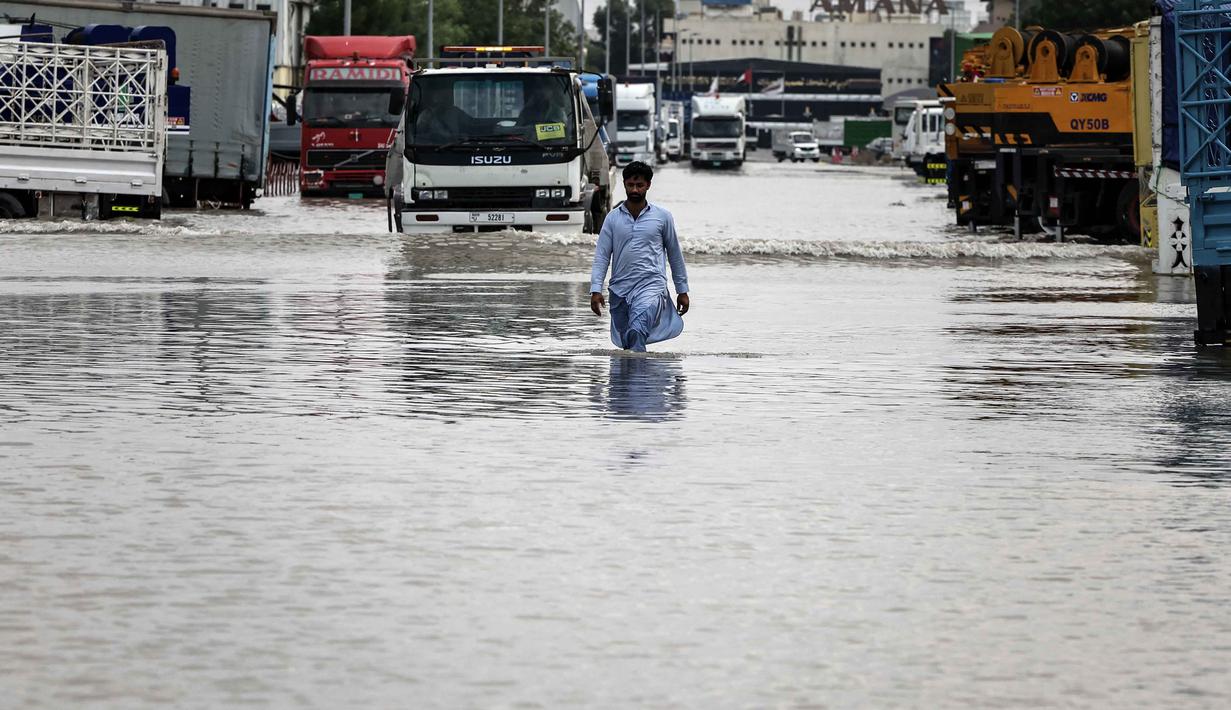 Hal ini dilakukan karena hujan lebat diperkirakan akan terjadi di negara gurun tersebut yang mengalami curah hujan rekor tahun lalu. Tampak dalam foto, seorang pria menerobos genangan air banjir setelah hujan lebat di Dubai, Uni Emirat Arab (UEA) pada Jumat 19 Desember 2025. (FADEL SENNA/AFP)