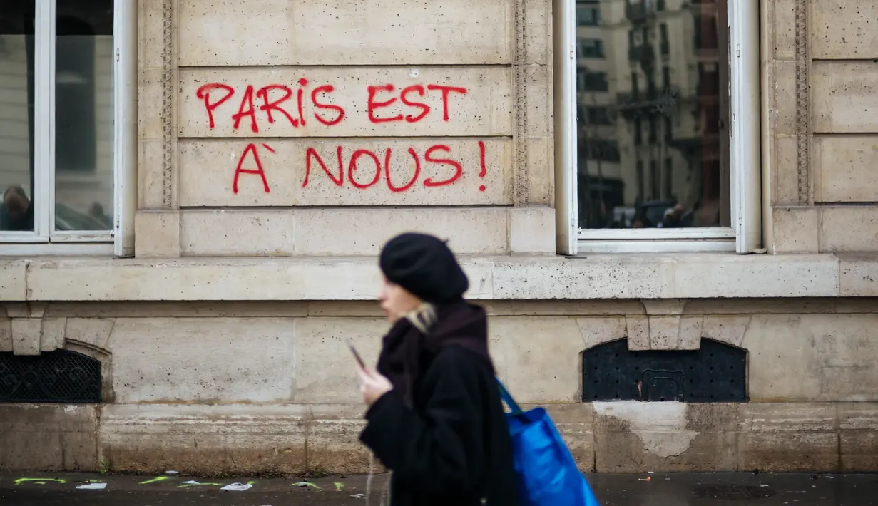 Seorang wanita berjalan melewati grafiti bertuliskan 'Paris adalah milik kita' dekat Arc de Triomphe, Paris, Prancis, Minggu (2/12). Pemrotes kenaikan pajak bahan bakar menandai Arc de Triomphe dengan grafiti berbagai warna. (AP Photo/Kamil Zihnioglu)