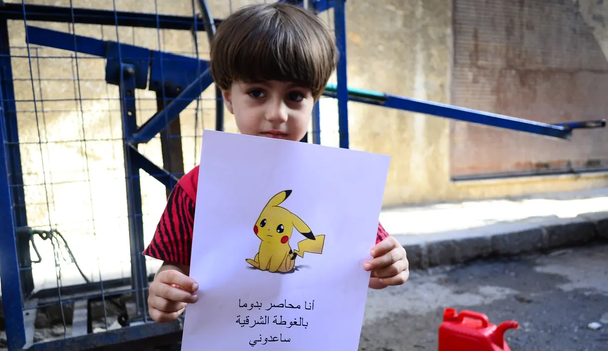 Seorang bocah memegang kertas bergambarkan karakter Pokemon serta tulisan "Aku terjebak di Douma di Timur Ghouta. Bantu aku", Suriah (22/7). (REUTERS)