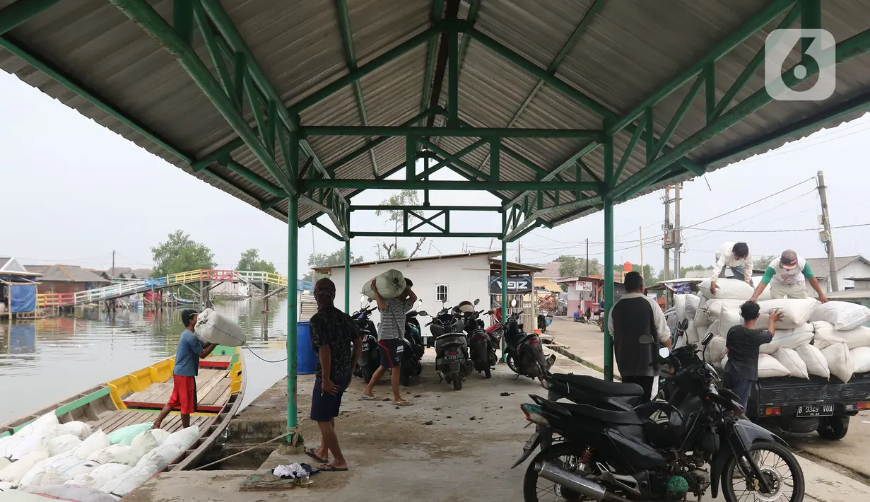 Pekerja mengangkut barang menggunakan perahu menuju dermaga di Desa Pantai Mekar, Muaragembong, Kabupaten Bekasi, Senin (6/12/2021). Jasa angkut barang menggunakan perahu tersebut banyak diminati warga untuk mempersingkat waktu perjalanan. (Liputan6.com/Herman Zakharia)