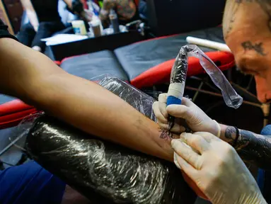 Seorang seniman tato membuat gambar lebah di pergelangan tangan seorang Mancunian di Manchester (28/5). Seniman ini membuat tato lebah untuk menggalang dana yang diberikan kepada korban serangan bom konser Ariana Grande. (AP Photo/Mstyslav Chernov)