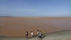 Pengunjung berjalan dipinggir pantai laut Espirito Santo yang airnya berubah menjadi cokelat di Brasil (22/11). Warna air berubah cokelat karena tambang milik Vale SA dan BHP Billiton jebol dan menumpahkan lumpur. (REUTERS/Ricardo Moraes)