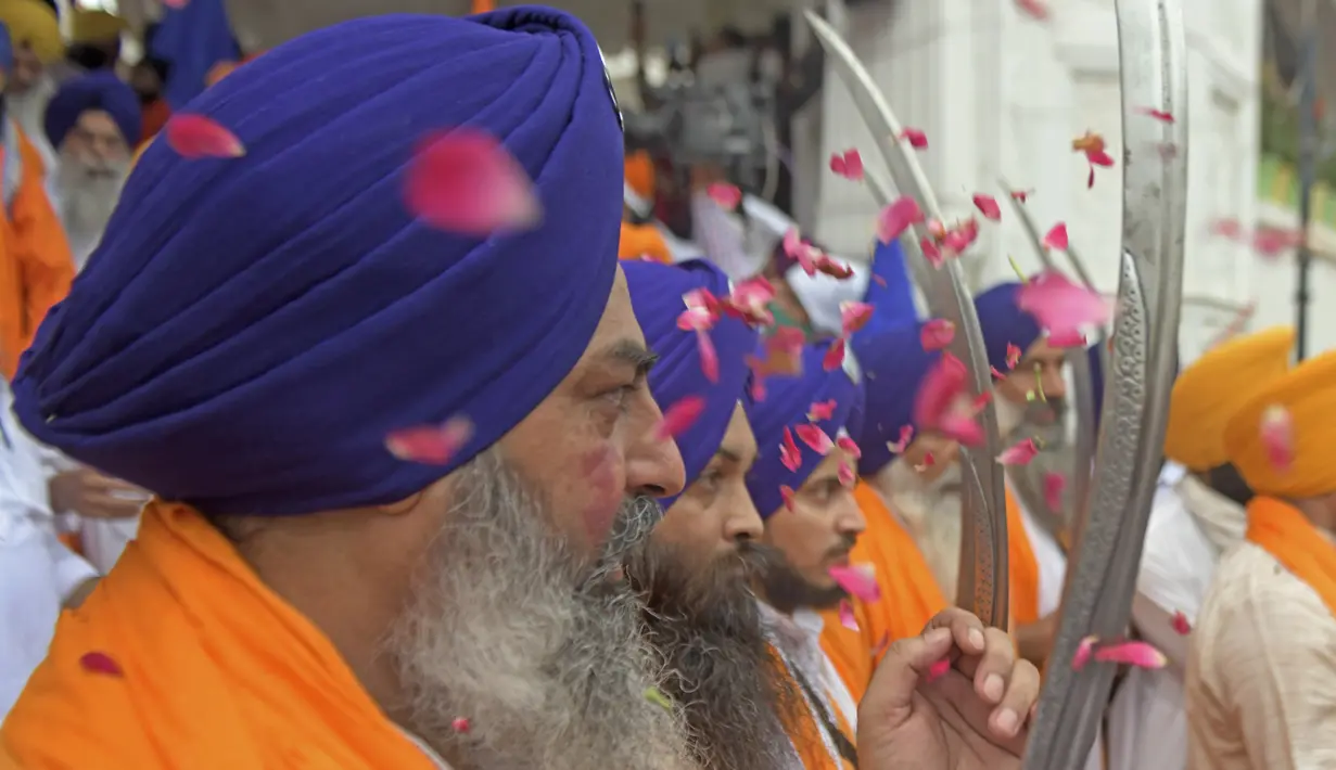 Umat Sikh yang dikenal sebagai 'Panj Pyare' memegang pedang selama prosesi keagamaan dari Gurudwara Ramsar ke Akal Takht Sahib di Kuil Emas, Amritsar, India, Rabu (19/8/2020). Acara ini untuk memperingati 416 tahun pelantikan Guru Granth Sahib. (NARINDER NANU/AFP)