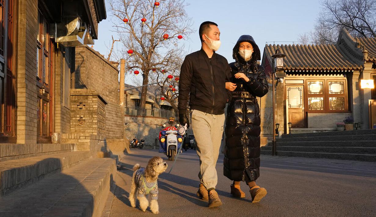 Warga yang mengenakan masker berjalan dengan anjing mereka di Beijing, China, Selasa (11/1/2022). Beijing dalam siaga tinggi menjelang Olimpiade Musim Dingin saat China mengunci kota ketiga di tempat lain akibat COVID-19. (AP Photo/Ng Han Guan)