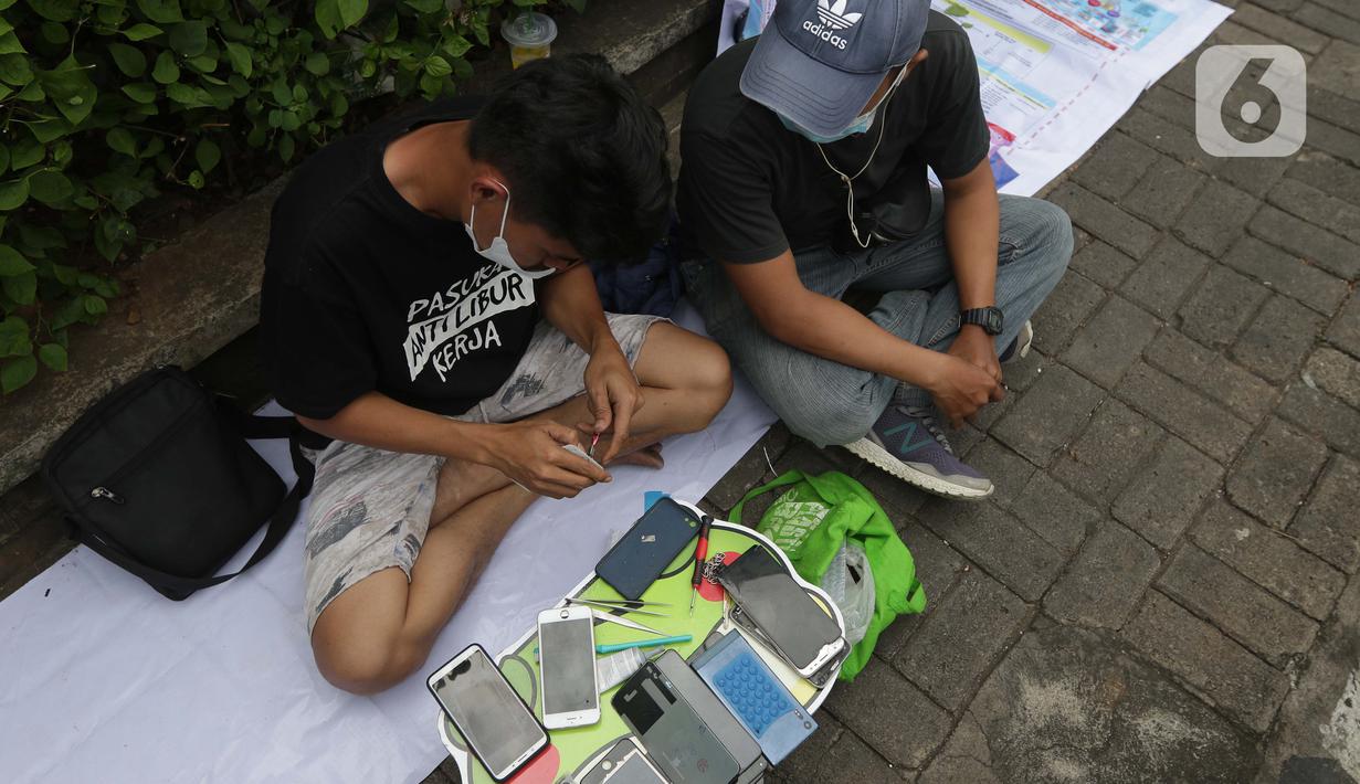 Penjual jasa perbaikan telepon genggam memperbaiki HP di trotoar jalan Mayjen Sutoyo depan Mall Pusat Grosir Cililitan (PGC), Jakarta, Rabu (14/7/2021). Kios yang biasa mereka tempati tutup seiring penutupan Mall PGC selama pemberlakuan PPKM Darurat Jawa-Bali. (Liputan6.com/Helmi Fithriansyah)