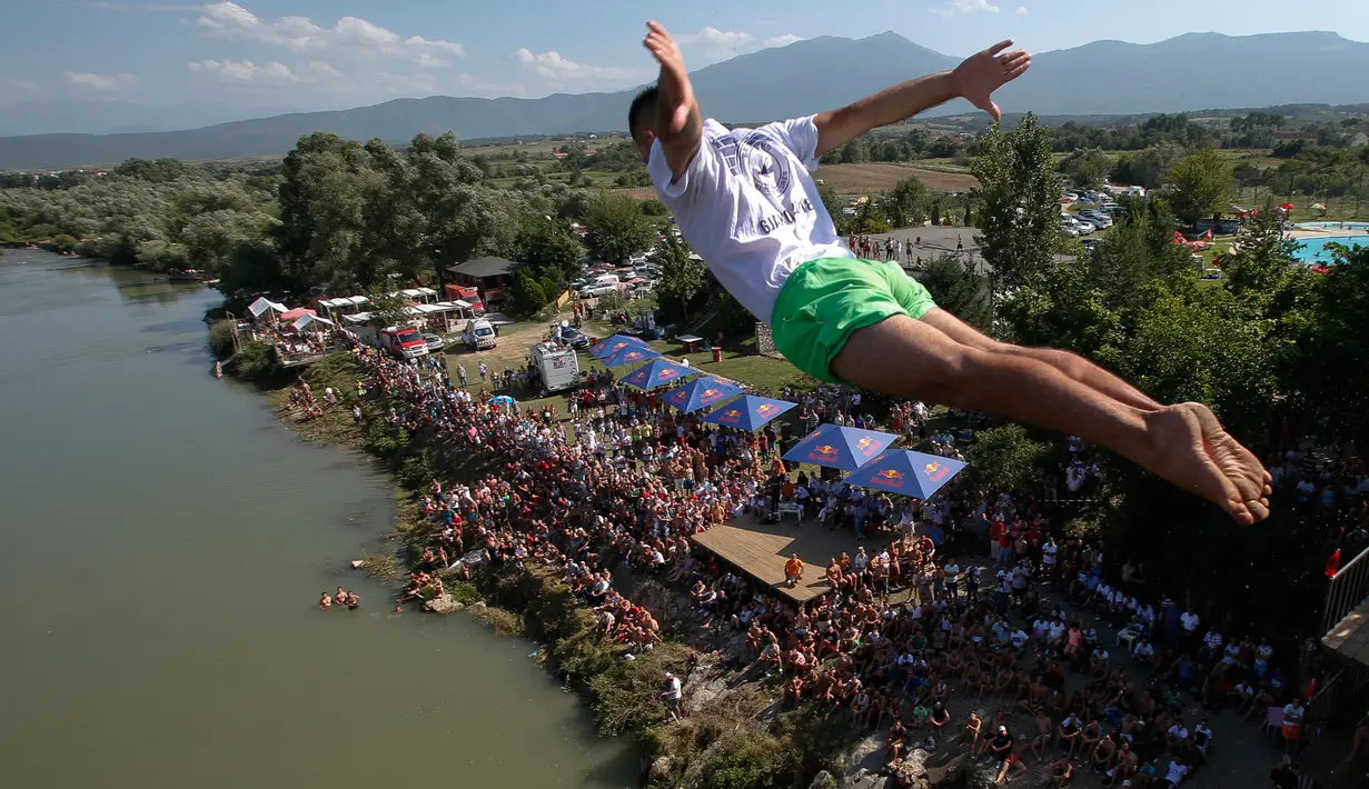 Penonton menyaksikan dari tepi sungai saat seorang peserta melakukan terjun bebas dari jembatan Ura e Shejnt dalam kompetisi menyelam tradisional ke-68 di Gjakova, Kosovo, 22 Juli 2018. Kompetisi ini dilakukan dari ketinggian 22 meter. (AP/Visar Kryeziu)