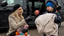 Pamela Anderson memberikan apel kepada seorang anak di pengungsian Grande-Synthe, Prancis (25/1). Memakai sepatu hak tinggi, Pamela membungkuk untuk memberikan buah, selimut, sarung tangan dan buku untuk anak-anak. (AFP/Philippe Huguen)
