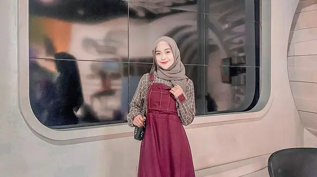 Gamis model overall warna merah kombinasi plaid long sleeve bikin tampilan terlihat manis. (Instagram/riaricis1795).