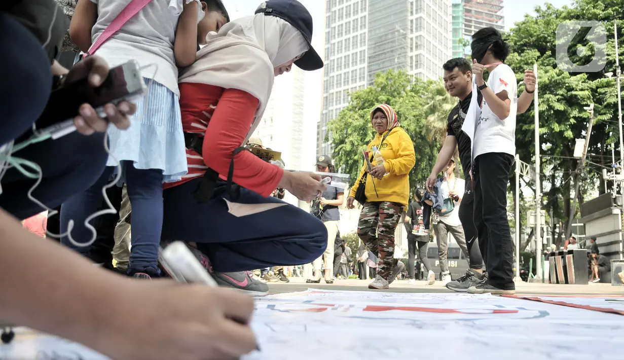 Warga membubuhkan tanda tangan saat berpartisipasi dalam peringatan Hari AIDS Sedunia di Bundaran HI, Jakarta, Minggu (1/12/2019). Kegiatan ini bertujuan mengedukasi masyarakat tentang penyakit AIDS dan mengajak untuk peduli serta tidak menjauhkan penderita AIDS. (merdeka.com/Iqbal S. Nugroho)