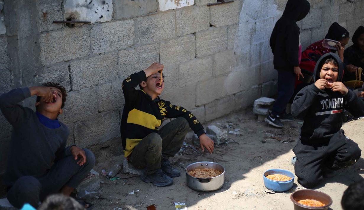 Situasi semakin memburuk ketika sejumlah lembaga bantuan mengurangi distribusi pasokan bahan pangan. World Central Kitchen disebut-sebut menghentikan pasokan tepung harian sebesar 20 hingga 30 ton. Tampak dalam foto, anak-anak pengungsi Palestina memakan makanan yang mereka terima dari dapur amal di kamp pengungsi Nuseirat, Jalur Gaza Tengah pada 13 April 2026. (Eyad Baba/AFP)