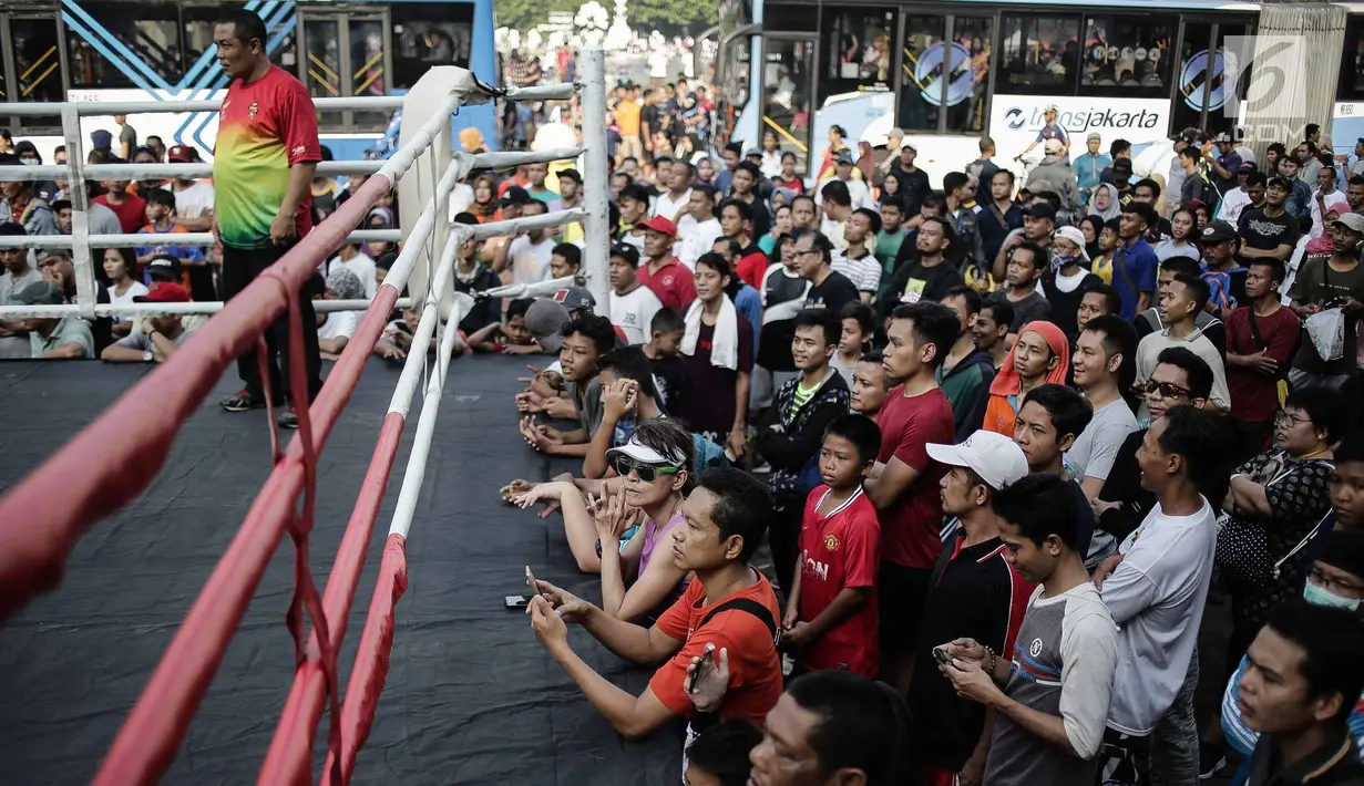 Warga menyaksikan pertandingan tinju amatir yang berlangsung saat Car Free Day di kawasan Bundaran HI, Jakarta, Minggu (29/4). Kegiatan ini merupakan pertandingan tanpa pemenang karena memakai konsep latih tanding. (Liputan6.com/Faizal Fanani)