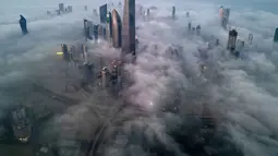 Pemandangan ini menciptakan ilusi kota di atas awan, dengan bagian atas gedung menembus kabut tebal. Tampak foto udara memperlihatkan gedung pencakar langit yang tertutup kabut pagi di Kota Kuwait pada Minggu 9 November 2025. (YASSER AL-ZAYYAT/AFP)