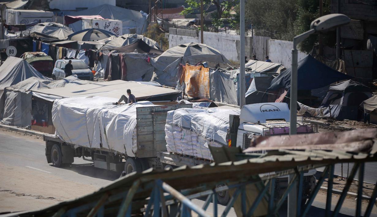 Truk-truk yang mengangkut bantuan yang masuk ke Jalur Gaza melalui pos perbatasan Karm Abu Salem, melintas di dekat tenda-tenda pengungsian di kamp pengungsi Nuseirat di bagian tengah Jalur Gaza, pada Selasa 14 Oktober 2025. (Eyad BABA/AFP)