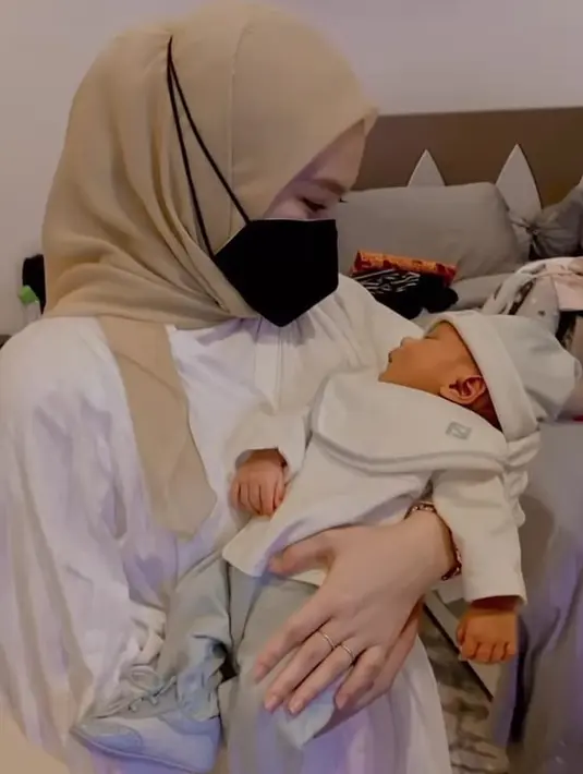 Melody pun tampil mengenakan pakaian putih yang dipadu padankan dengan kerudung segitu warna kuningnya. Mantan JKT48 ini terlihat menggendong baby L.  Instagram/@daidermawann