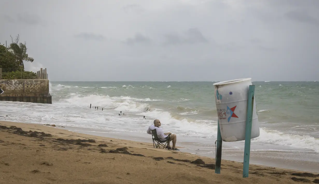 Seorang pria duduk di depan pantai menyaksikan ombak pecah sebelum kedatangan Badai Tropis Fiona di San Juan, Puerto Rico, Sabtu (17/9/2022). Fiona diperkirakan akan menjadi badai saat mendekati Puerto Rico dan akan melintasi wilayah teritori Amerika Serikat pada Minggu pagi. (AP Photo/Alejandro Granadillo)