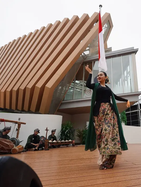 Kebaya hitam-nya dipadukan dengan kain batik bermotif bunga penuh warna dan selendang hijau menjuntai, menciptakan siluet yang elegan sekaligus membumi.   [@arieltatum].