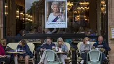 Orang-orang duduk di bar teras di sebelah potret Ratu Elizabeth II di pusat kota London pada 13 September 2022. Hotel, restoran, dan toko-toko penuh sesak saat penggemar kerajaan berdatangan ke jantung kota London untuk melihat jalan-jalan yang dipagari bendera, prosesi yang dipenuhi kemegahan, dan berani mengantre sejauh bermil-mil untuk kesempatan sekali seumur hidup mengucapkan selamat tinggal kepada Ratu Elizabeth II. (AP Photo/Emilio Morenatti, File)