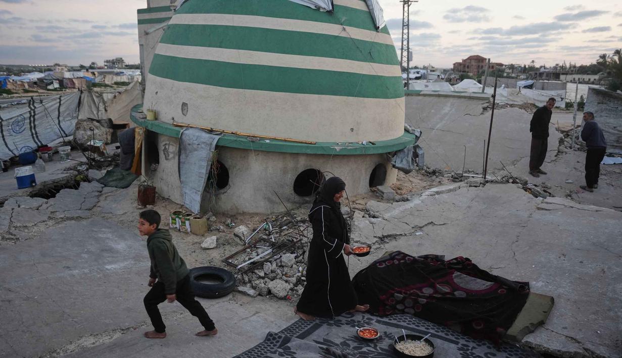 Mereka larut dalam kebersamaan yang penuh haru dan sukacita meski berada di tengah reruntuhan akibat konflik yang berkepanjangan. Tampak dalam foto, Khadija Suleiman menyiapkan makanan untuk iftar keluarganya, yaitu hidangan berbuka puasa selama bulan suci Ramadhan, di reruntuhan masjid tempat mereka saat ini berlindung di Deir al-Balah, Jalur Gaza, Jumat 6 Maret 2026. (AP Photo/Abdel Kareem Hana)