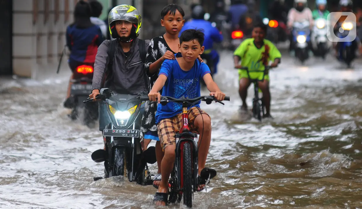 Anak-anak mengendarai sepeda melintasi banjir yang merendam Jalan Benteng,  Duta Kranji, Kalibaru, Bekasi, Jawa Barat, Jumat (24/2/2023). Jalan yang dilalui oleh para pengendara masih digenangi air ditambah dari luapan kalibaru Duta Kranji akibat hujan deras yang mengguyur Kota Bekasi sejak Kamis (23/2/2023) malam. (merdeka.com/Imam Buhori)