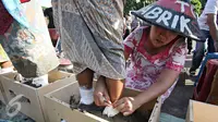 Seorang perempuan membantu temannya menyemen kaki saat aksi di depan Istana Negara, Jakarta, Selasa (12/4). Aksi tersebut merupakan bentuk protes atas pembangunan pabrik semen di wilayah mereka. (Liputan6.com/Immanuel Antonius) 
