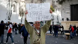 Pria paruh baya membawa papan berisi “Macri, hentikan!” dalam bahasa Spanyol saat demonstrasi di Plaza de Mayo, Buenos Aires, Argentina, Selasa (22/8). Macri berusaha menurunkan upah para buruh demi menghasilkan Investasi lebih. (Victor R. Caivano/AP)