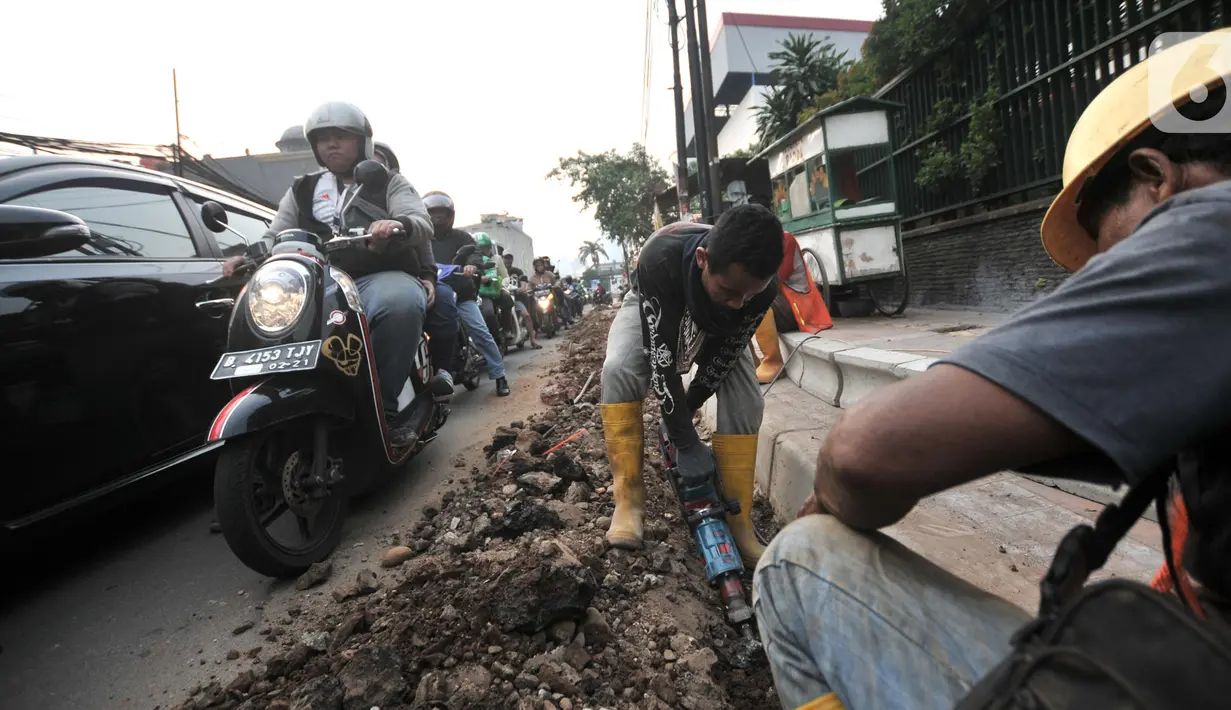 Pengendara melintas dekat pekerja yang tengah menyelesaikan proyek revitalisasi trotoar di Jalan Tebet Raya, Jakarta, Selasa (5/11/2019). Adanya proyek revitalisasi trotoar tersebut mengakibatkan kemacetan di kawasan itu semakin parah, terlebih saat jam sibuk. (merdeka.com/Iqbal Nugroho)