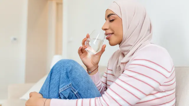 Seorang wanita muslimah mengenakan jilbab pink sedang minum air putih (Foto Dok: Freepik/ stefamerpik)