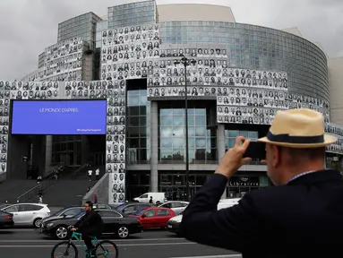 Seorang pria mengambil gambar potret para petugas kesehatan yang ditempelkan di bagian depan Bastille Opera di Paris, Prancis, Jumat (10/7/2020). Potret hitam putih itu untuk memberi penghormatan kepada pekerja medis yang berjuang menghadapi Corona Covid-19. (AP Photo/Francois Mori)
