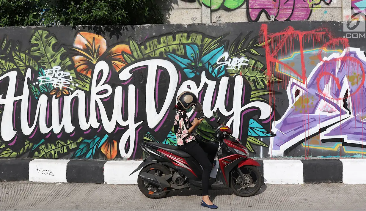 Pengendara berhenti di jalur inspeksi Sungai Ciliwung, Jakarta, Kamis (27/12). Mural yang dibuat oleh beberapa komunitas tersebut menjadikan jalur inspeksi Sungai Ciliwung tampak lebih berwarna dan asri. (Liputan6.com/Immanuel Antonius)