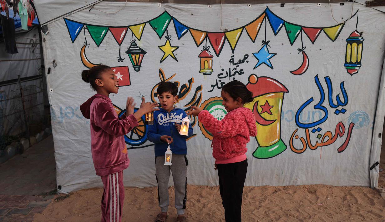 Beberapa anak tampak antusias menggantung hiasan sederhana di antara tali-tali penyangga tenda. Tampak dalam foto, para pengungsi muda Palestina bermain dengan lampion Ramadan saat dekorasi dipasang di samping tenda mereka di kamp pengungsi Bureij di Jalur Gaza tengah pada 15 Februari 2026. (Eyad Baba/AFP)