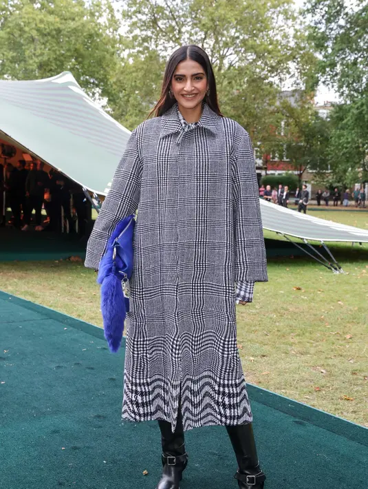 Aktris Sonam Kapoor tampil chic mengenakan checkered print midi dress abu-abu dipadukan trench coat matching dan leggings. [Dok/Burberry]