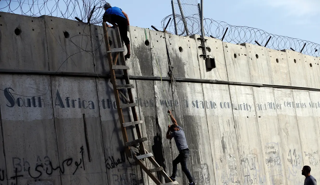 Pemuda Palestina menggunakan tangga berusaha memanjat tembok pembatas Israel di sebelah pos pemeriksaan Qalandia di Tepi Barat saat berangkat untuk beribadah salat Jumat di Masjid Al-Aqsa, Yerusalem, Jumat (9/6). (AFP Photo/Abbas Momani)