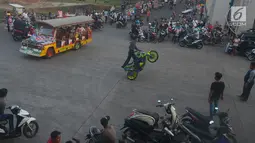 Sebuah mobil odong-odong melintas di tengah atraksi para freestyle di kawasan Kanal Banjir Timur, Jakarta, Selasa (29/5). Aksi berbahaya para rider di atas sepeda motor ini dilakukan pada saat ngabuburit menunggu bedug berbuka. (Merdeka.com/Imam Buhori)