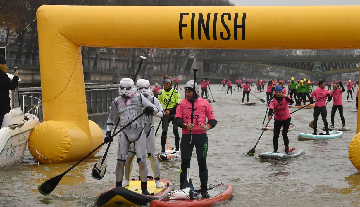 Peserta berkostum Star Wars Stormtrooper mencapai garis finis lomba dayung sambil berdiri pada Nautic SUP Paris di sungai Seine, Paris, Minggu (3/12). Nautic SUP Paris merupakan lomba dayung sambil berdiri terbesar di dunia. (AFP PHOTO/CHRISTOPHE SIMON)
