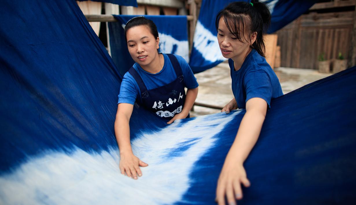 Dua perempuan menghaluskan permukaan kain di sebuah bengkel kerja di Desa Etnis Dong Fengdeng di Wilayah Rongjiang, Provinsi Guizhou, China, 6 September 2020. Warga setempat memanfaatkan kondisi cuaca musim gugur yang mendukung untuk membuat kain tradisional kelompok etnis Dong. (Xinhua/Liu Xu)