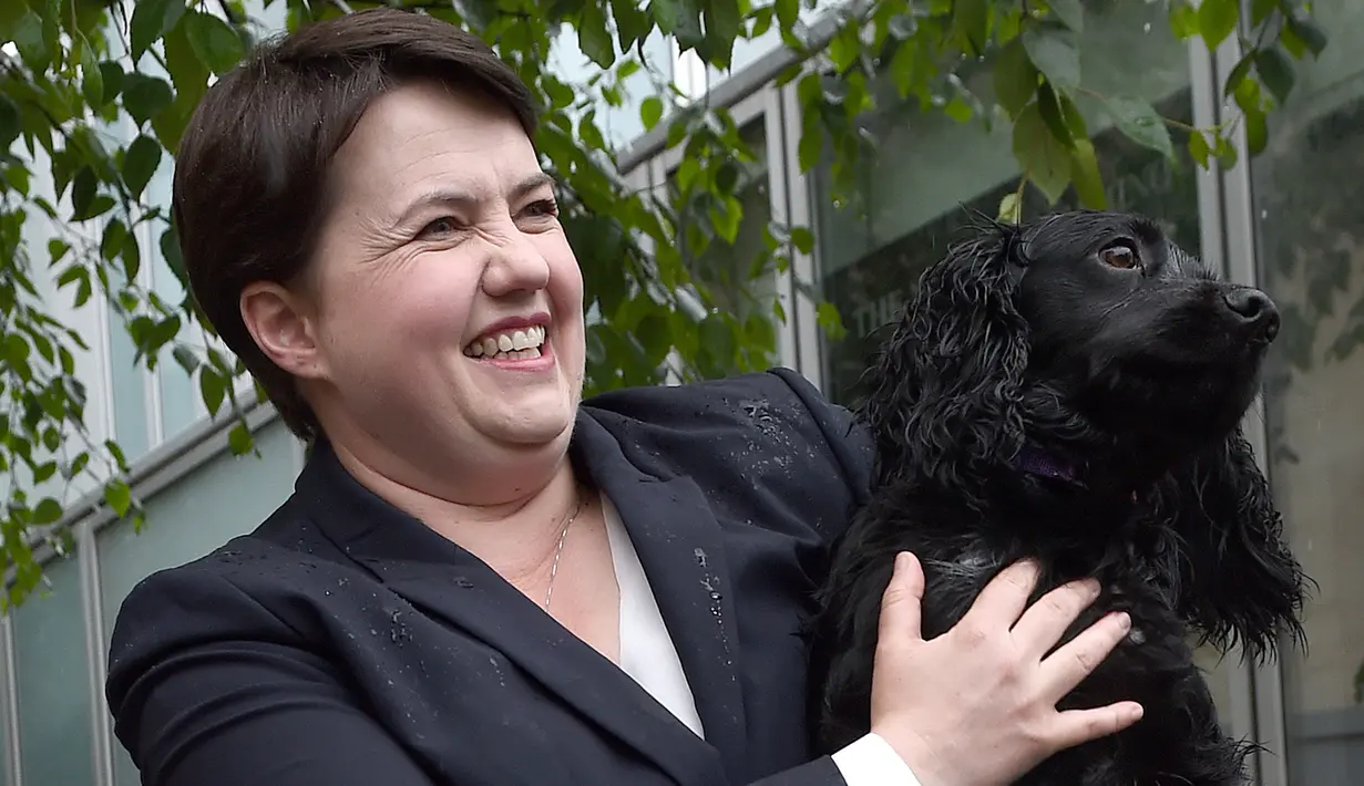 Pimpinan partai Konservatif Skotlandia, Ruth Davidson berpose bersama anjingnya di luar kafe yang dijadikan TPS di Edinburgh, Kamis (8/6). Para pemilih mengajak anjingnya untuk menemani mereka mengambil bagian dalam Pemilu Inggris. (Lesley Martin/AFP)