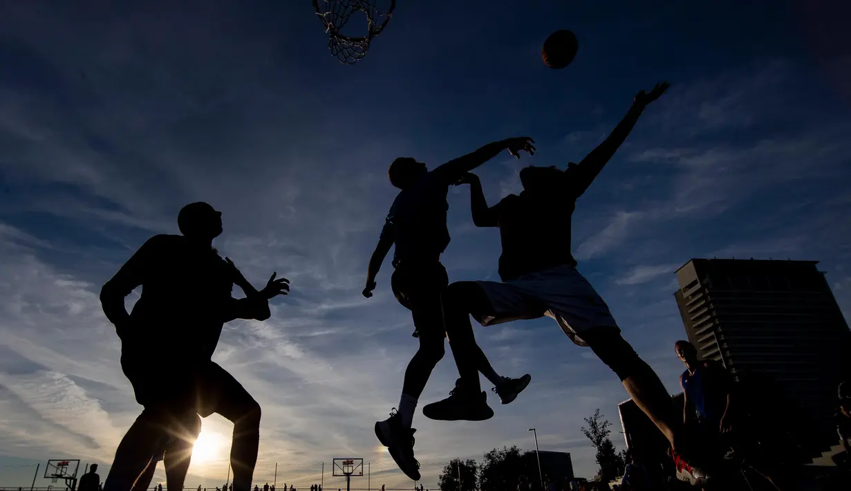 Orang-orang bermain bola basket saat matahari terbenam di sebuah lapangan di pusat Vilnius, Lithuania, Rabu, (15/7 2020). (AP Photo/Mindaugas Kulbis)
 