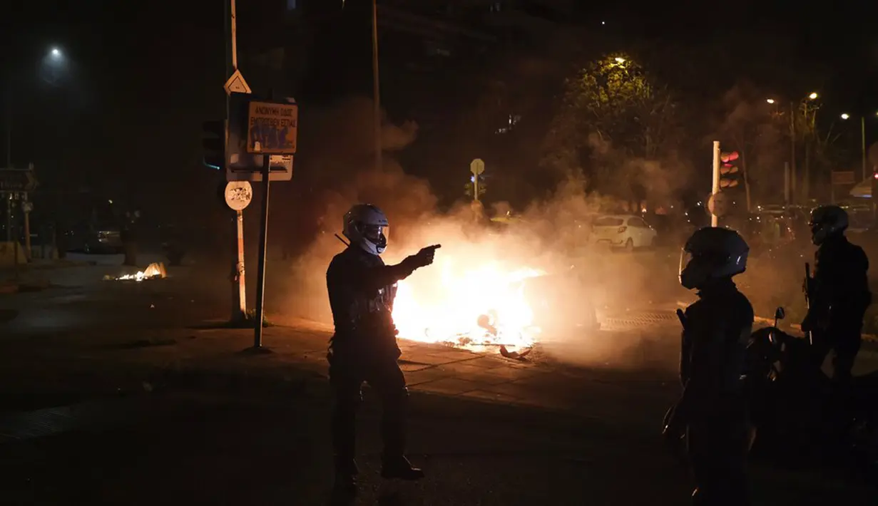 Seorang polisi memberi isyarat saat tempat sampah terbakar dalam bentrokan dengan pengunjuk rasa di Athena, Yunani, Selasa (9/3/2021). Bentrokan parah terjadi di Athena setelah pemuda yang memprotes insiden kekerasan polisi menyerang kantor polisi dengan bom bensin. (AP Photo/Aggelos Barai)