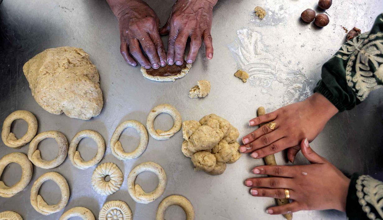 Akan tetapi ciri khasnya yang berbentuk cincin dan dipenuhi taburan biji wijen tetap ada di berbagai wilayah berbeda. Tampak dalam foto, para wanita menyiapkan biskuit tradisional "kaak" yang berbentuk cincin menjelang Idul Fitri, hari raya yang menandai berakhirnya bulan puasa suci Ramadan, di Kota Gaza pada 16 Maret 2026. (Omar AL-QATTAA/AFP)