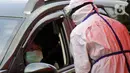 Petugas berpakaian APD lengkap melayani pasien yang secara mandiri melakukan swab test drive thru di halaman parkir rumah sakit di Jakarta, Rabu (12/5/2020). Swab test drive thru dilakukan untuk mendeteksi dan mencegah penyebaran virus corona COVID-19. (Liputan6.com/Johan Tallo)