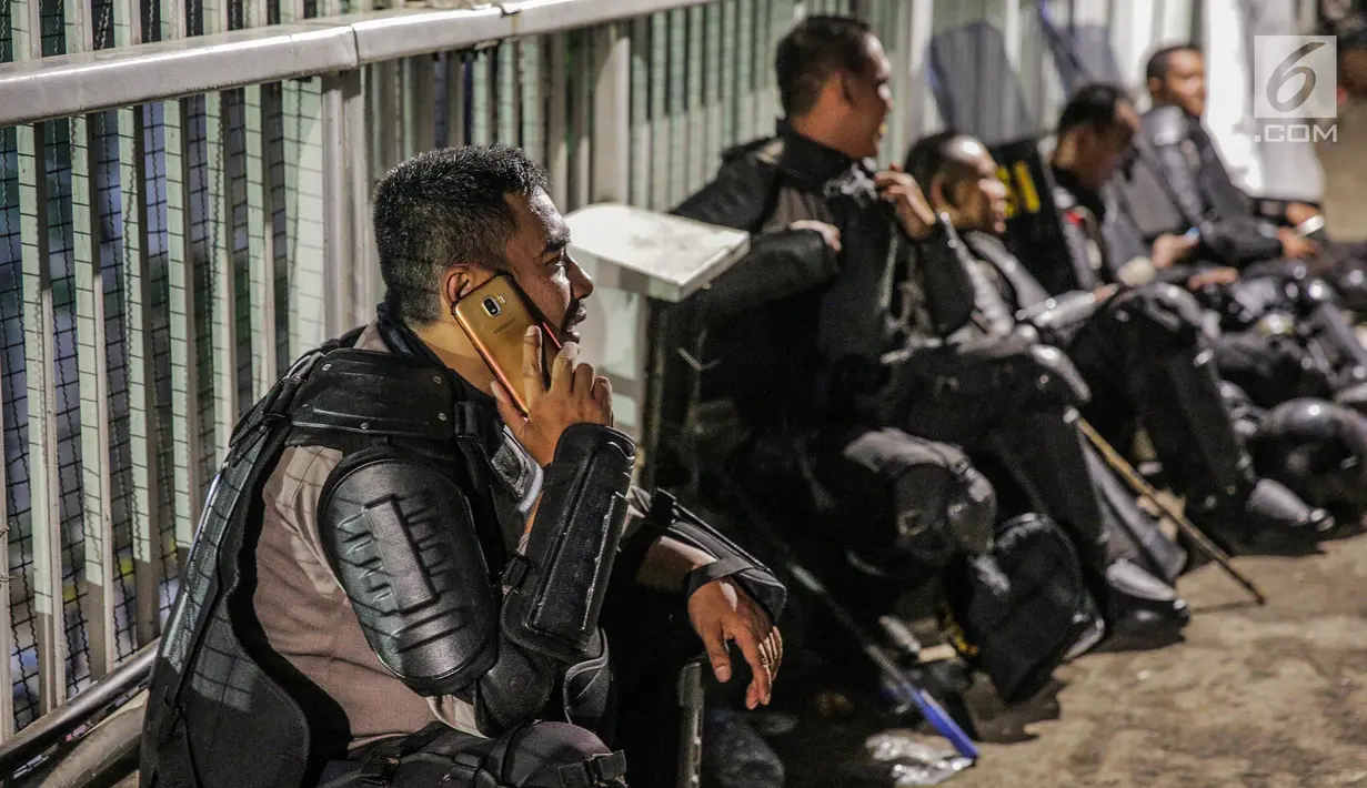 Aparat kepolisan menggunakan telepon genggamnya saat melepas lelah di jembatan penyeberangan orang (JPO) depan Gedung DPR, Jakarta, Selasa (24/9/2019). Mereka melepas lelah usai mengawal demonstrasi mahasiswa menolak pengesahan RUU KUHP dan revisi UU KPK. (Liputan6.com/Faizal Fanani)
